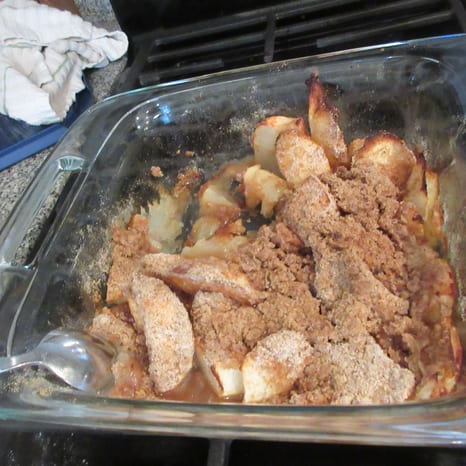 A baking dish of apple crisp with a browned oat topping and one serving scooped out