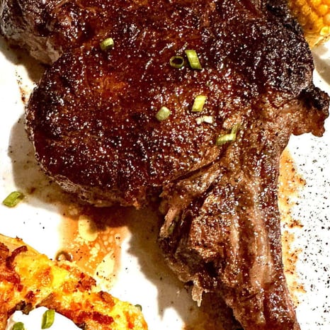 Sliced bone-in ribeye with twice-baked potatoes, corn, and broccoli on a dinner plate
