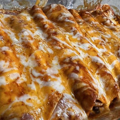 A baking dish of cheese enchiladas in red chile sauce, finished with sour cream and green onion