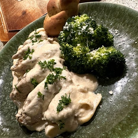 Sliced pan-seared chicken breast in a creamy Parmesan sauce over fettuccine, served with a roasted potato and Parmesan-topped broccoli