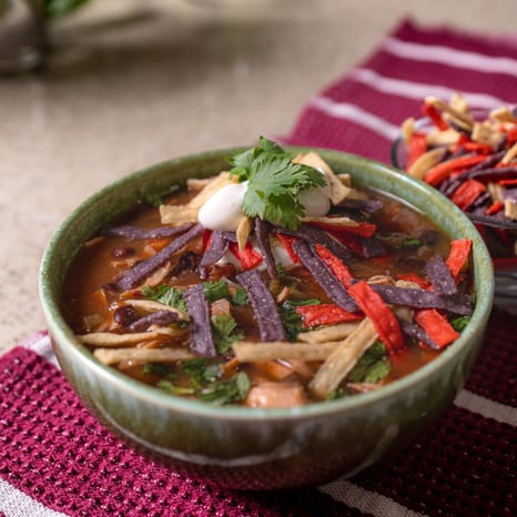 A bowl of chicken tortilla soup topped with tortilla strips, sour cream, and cilantro