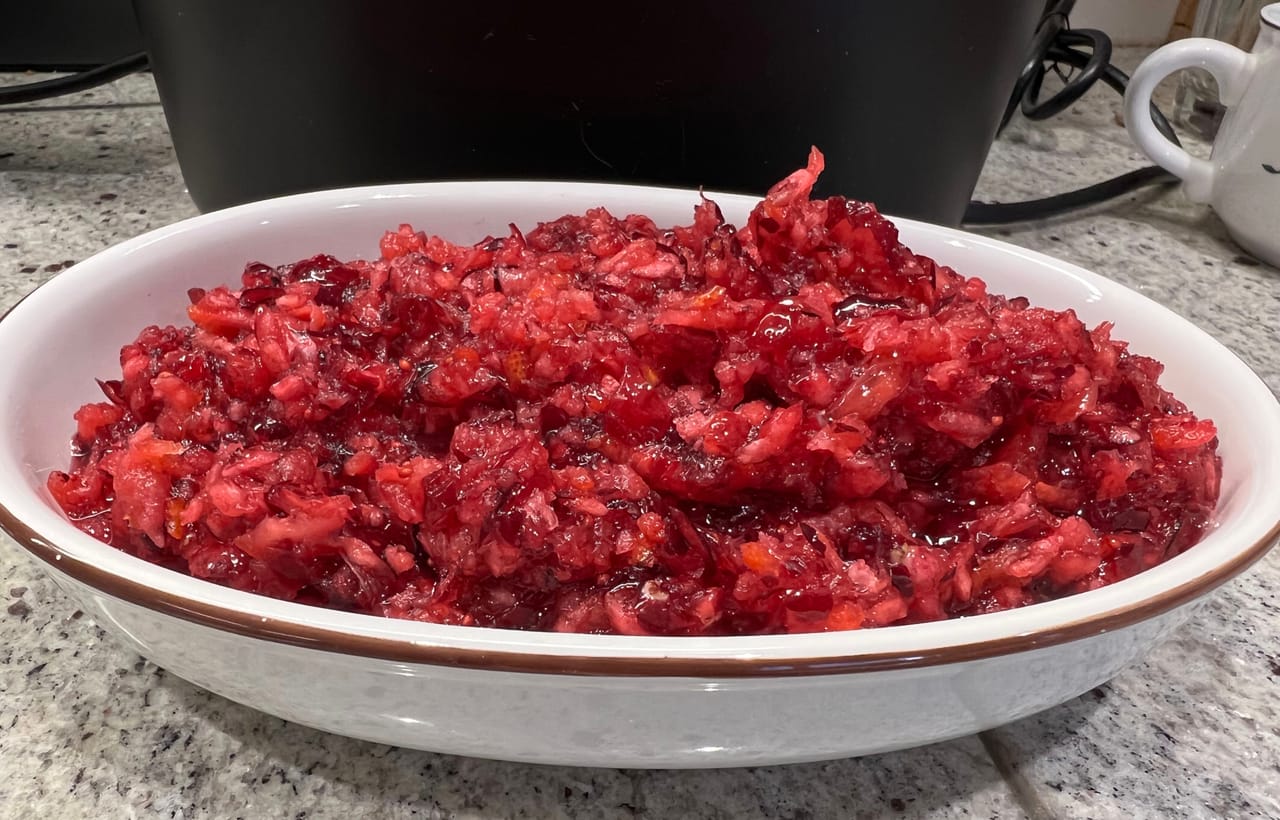 A bowl of whole-berry cranberry sauce beside sliced roast turkey