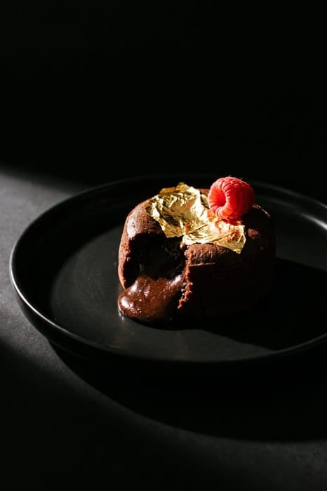Dark chocolate lava cake cut open with molten center, fresh raspberries and red raspberry sauce