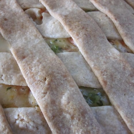 A deep-dish chicken pot pie with a golden puff pastry lid, one slice served on a green plate