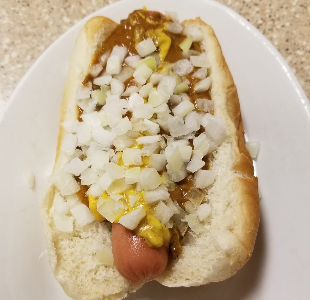 A Detroit Coney dog in a bun, topped with chili, yellow mustard, and chopped onion