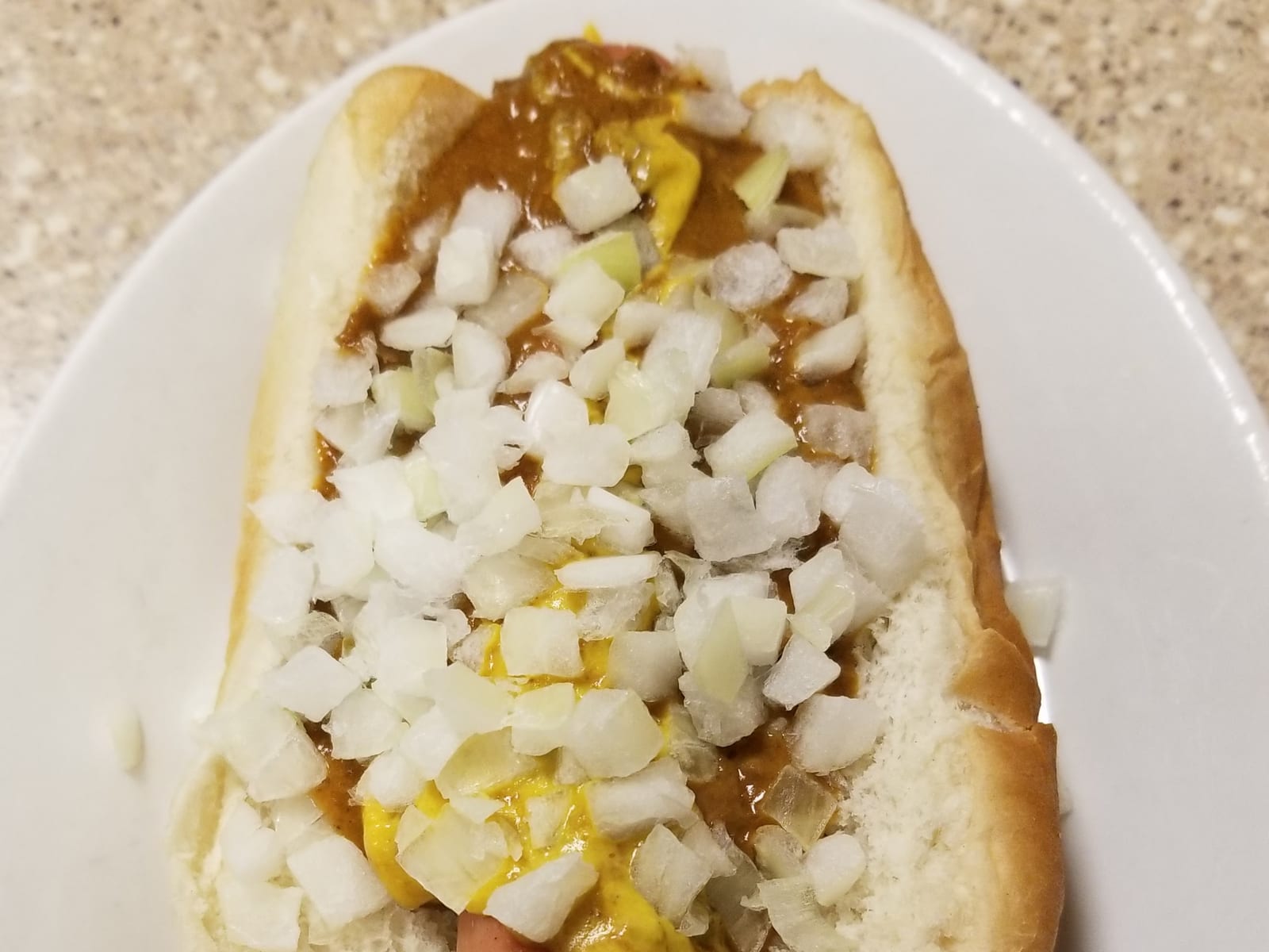 A Detroit Coney dog in a bun, topped with chili, yellow mustard, and chopped onion