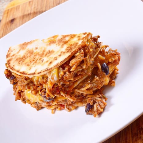 Cross-section of a stacked ground beef and Spanish rice quesadilla, its grilled tortilla layers oozing melted cheese and studded with black beans, on a white plate