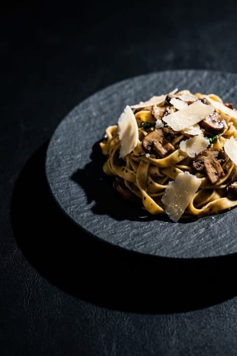 Nest of fresh tagliatelle with browned wild mushrooms, grated Parmigiano and thyme on a dark plate