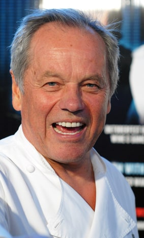 Wolfgang Puck laughing, wearing a white chef's coat at a press event