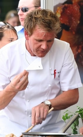 Gordon Ramsay concentrating while seasoning a dish at an outdoor cooking demonstration