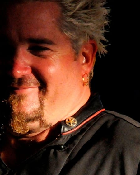 Guy Fieri in a white chef's coat at a grill during a cooking demonstration