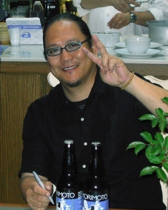Masaharu Morimoto seated at a table in a restaurant, smiling, photographed in the mid-2000s