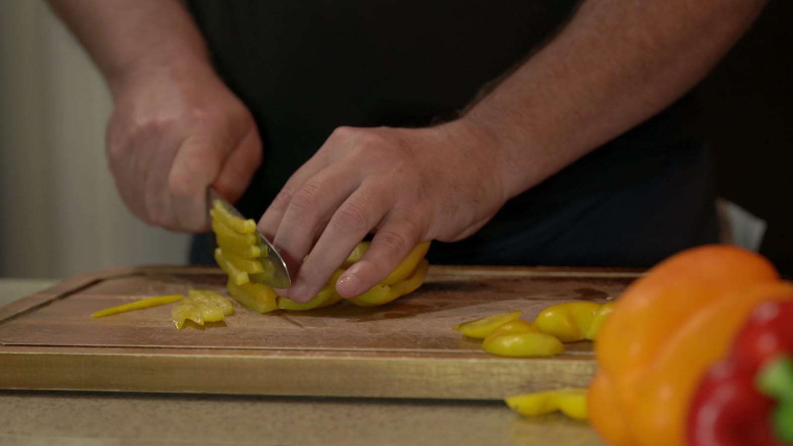 Close-up of hands julienning a yellow bell pepper on a wooden board