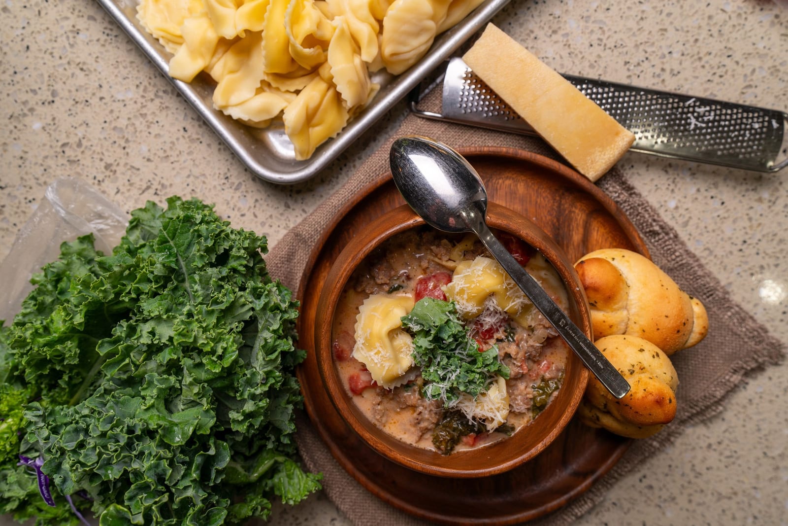 Wide overhead table: soup pot, kale, pasta, cheese grater