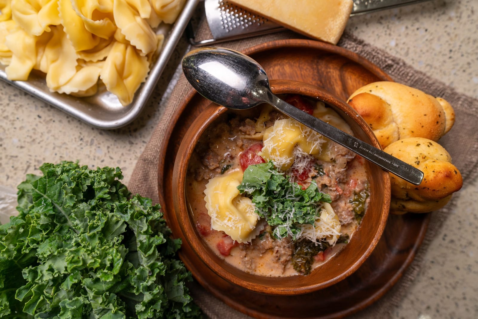 Overhead tortellini soup with kale, pasta, rolls on wood