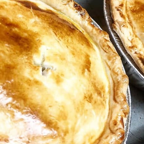 Two individual chicken pot pies in foil pans with deep golden, glossy puff pastry lids and a steam vent cut in the center