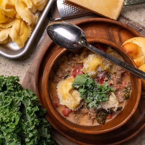 Overhead view of sausage, kale and tortellini soup with garlic knots and Parmesan