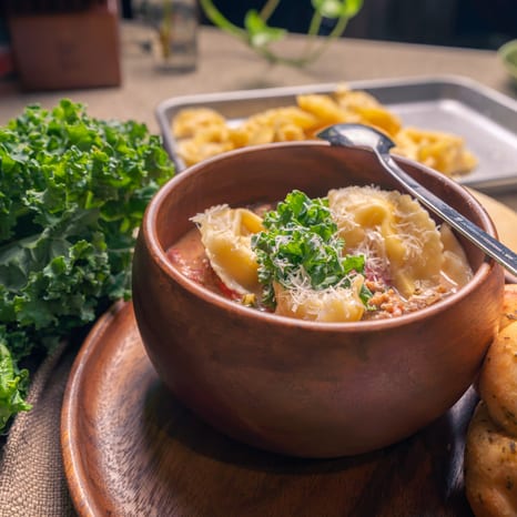 Bowl of Italian sausage, kale and tortellini soup on a wooden plate, side view