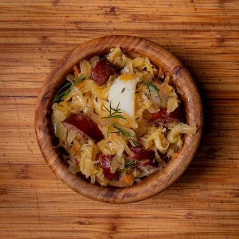 Skillet of braised sauerkraut and cabbage with seared kielbasa rounds and soft potato chunks, topped with fresh dill
