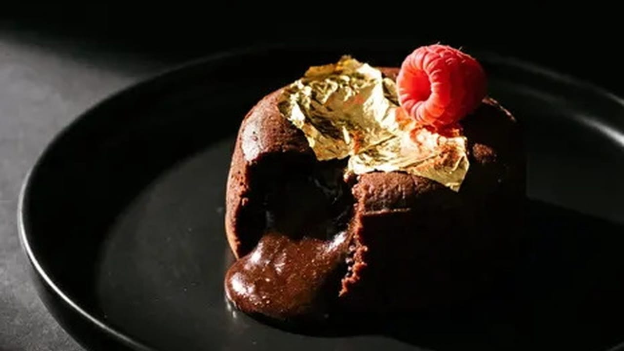 Two molten chocolate fondants on a white plate, one broken open with a spoon so the center runs