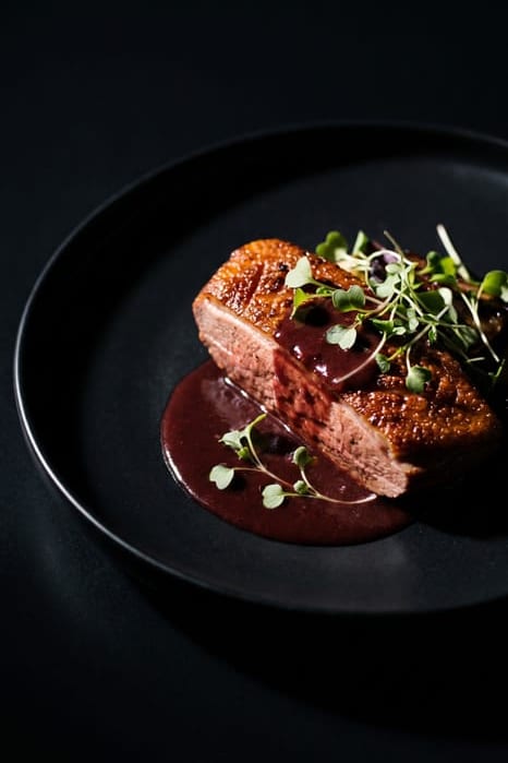 Sliced seared duck breast with crisp golden skin and pink center, drizzled with dark red wine sauce