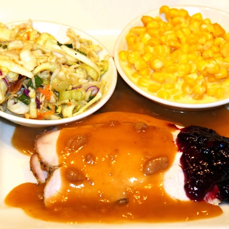 Sliced roast turkey in brown gravy, with cranberry sauce, creamed corn, and coleslaw